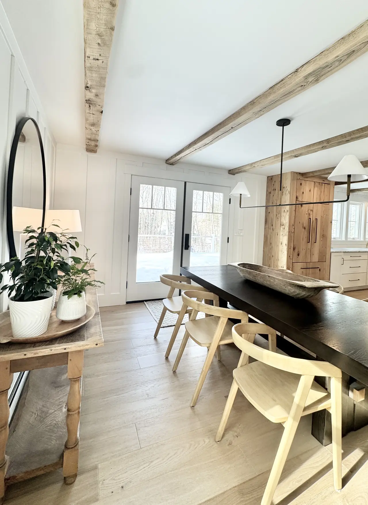 A dining room with an exposed beam, wood table, and coastal light in Arundel, Maine