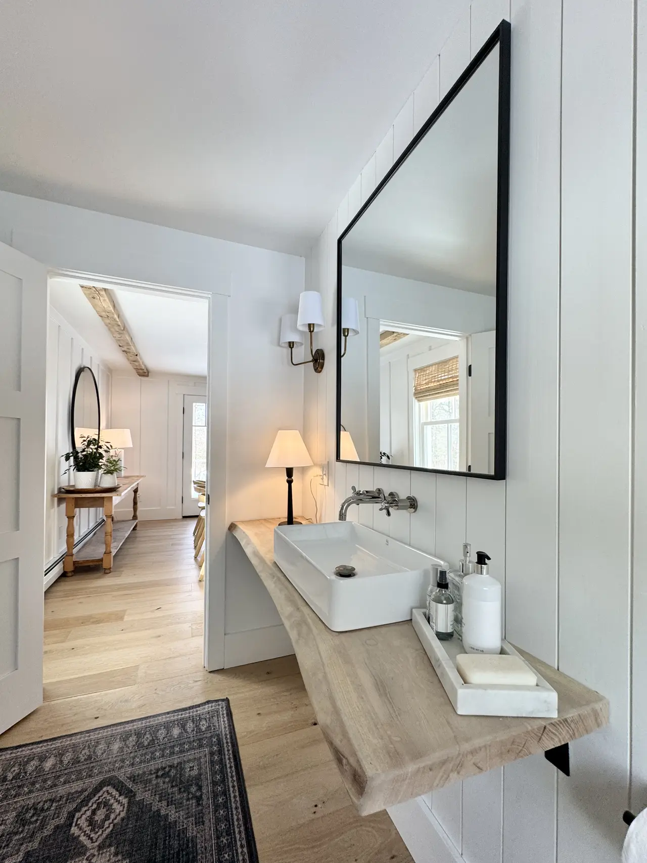 A vanity with a round mirror, sconce, and layered rug