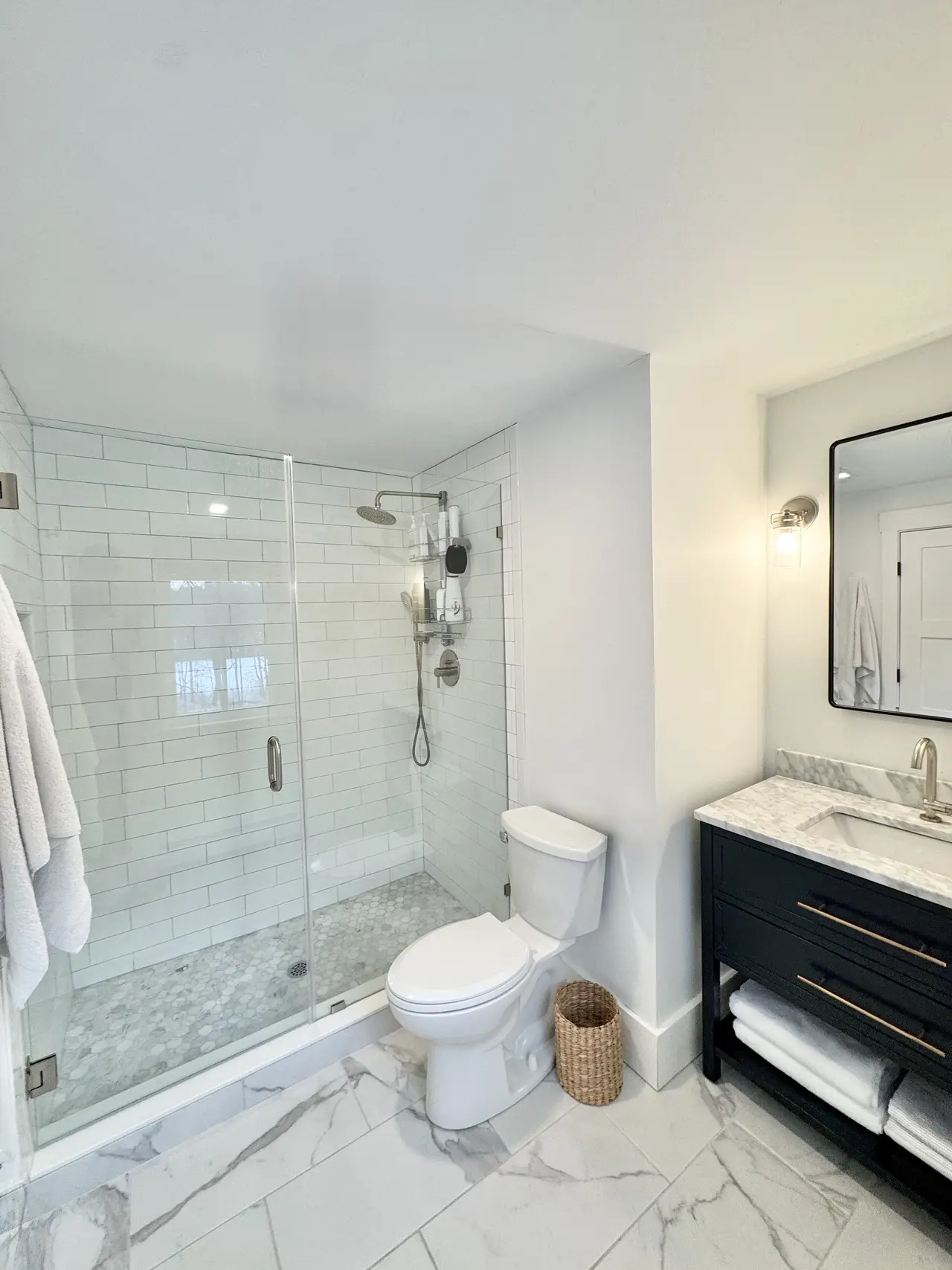 A marble shower and dark vanity in a guest bath