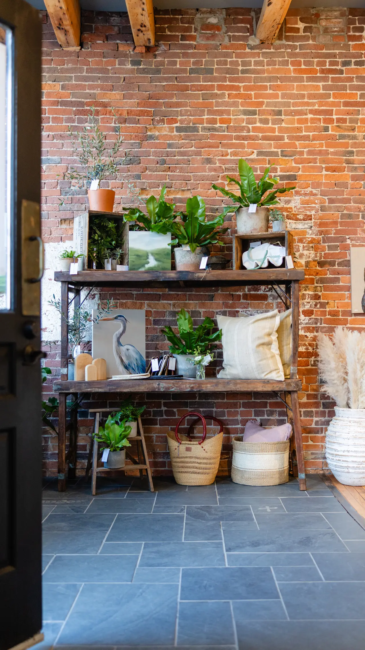 A STELLAN shelf against exposed brick: plants, original art, pillows, and baskets
