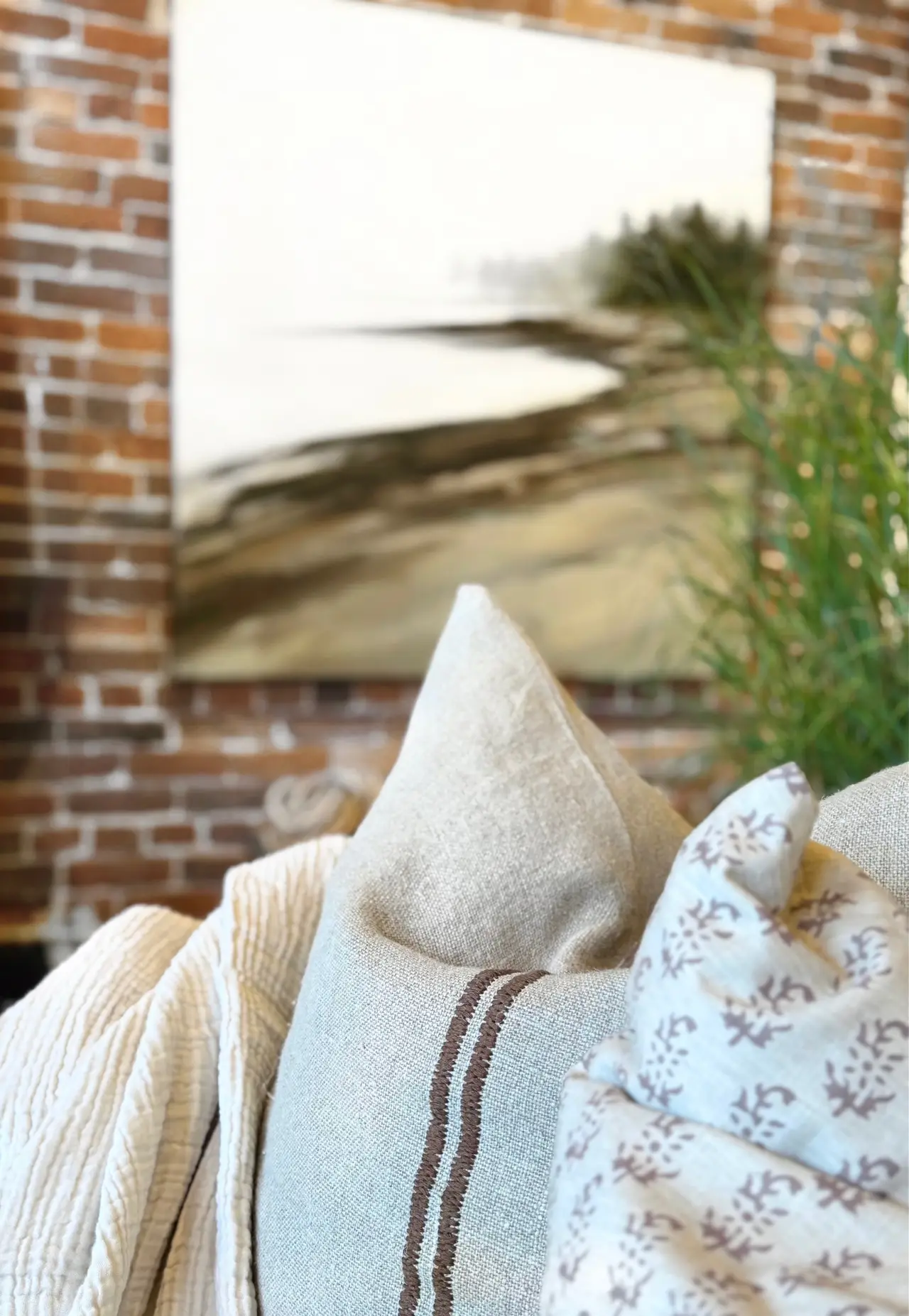 A styled corner: exposed brick, a framed coastal painting, and layered pillows