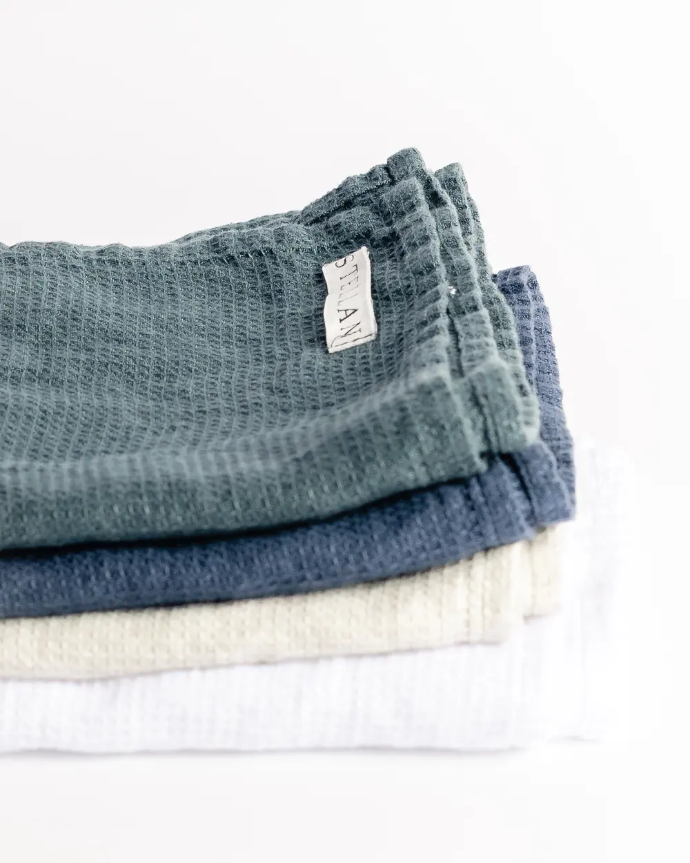 A folded stack of STELLAN waffle-weave throws in sage, navy, cream, and white